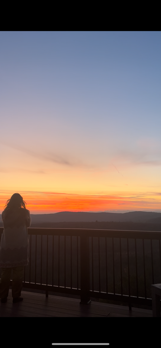 Liv stands on a deck looking at a sunset
